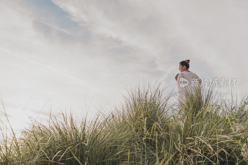 一名女子站在英国康沃尔郡Gwithian Towans海滩的沙丘上，享受着夏末的阳光。